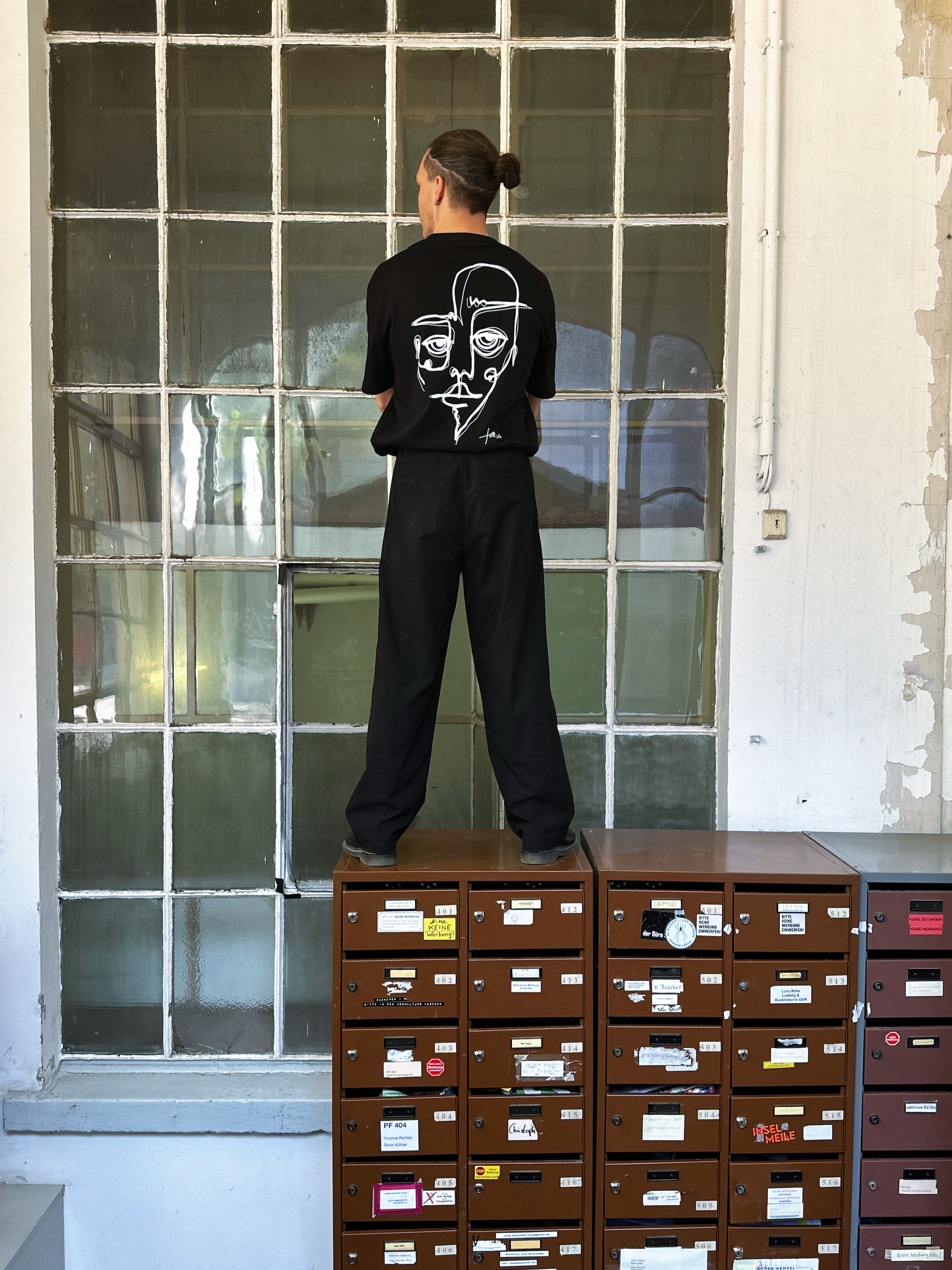 Schwarzes oversized T-Shirt mit weißem, abstrakten Gesichtslinien-Design auf dem Rücken und „faies“-Schriftzug – minimalistischer Streetwear-Stil auf schwarzem Hintergrund.